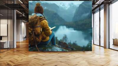 A woman with a backpack sits on a rock. Wall mural