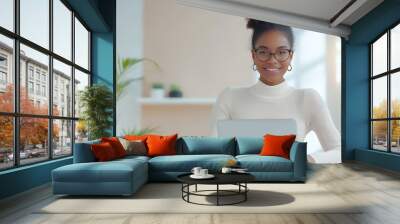 a smiling businesswoman working on a laptop in a clean, minimalistic office, soft lighting Wall mural