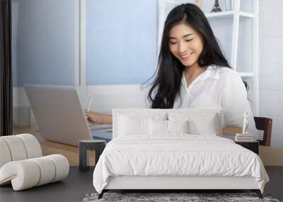 Education study abroad,Asian student girl sitting at table looking book while do homework with laptop making video call abroad using internet friend connection, happy mood smiling broadly in library Wall mural