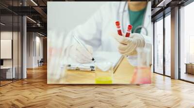 hands a medical doctor holding blood sample and making notes writing on prescription,lab technician hold blood tube test background of test tubes microscope blood samples other patients in laboratory Wall mural