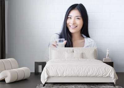 Happy young Asian woman drinking milk from the glass after exercise.over white background, shake looking at camera in the living room at home Wall mural