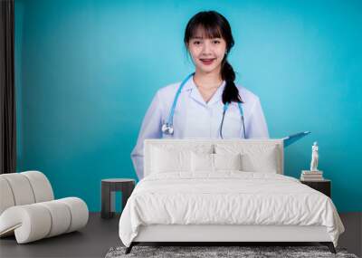 young Asian braces Doctor in a white coat holding blue folder and looking at camera while making a visit to the patient, Smiling woman physician pharmacies a white coat over isolated blue background Wall mural