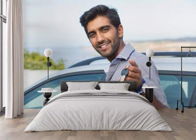 Closeup portrait happy, smiling, young man, buyer showing keys of his new car isolated outside dealership lot. Personal transportation, auto purchase concept Wall mural