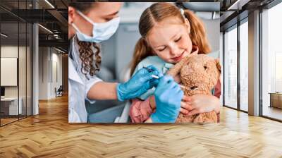 At the doctor's appointment. A child is sitting in a dental chair and holding a toy rabbit and a nurse is playfully examining the toy. Approach to the patient. Wall mural