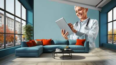 Beautiful female medic working with a digital tablet on a blue background. Family doctor. Wall mural