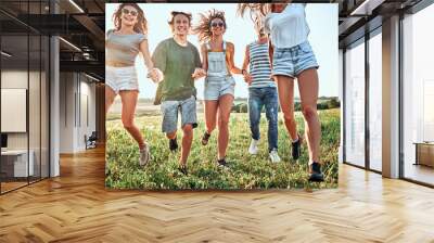 Big group of happy friends run and jump at sunset field against sunshine Wall mural