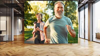 Cardio training. Close up of energetic fit sportsman spending morning in park and jogging together with wife. Active pensioners taking care of health and doing regular physical activities on nature. Wall mural