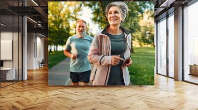 Cardio workout concept. Spirited sport couple jogging in morning in urban park during sunny day. Senior man and woman in activewear keeping in shape through regular training. Wall mural