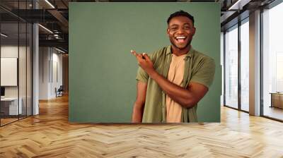 Choose this. African american male person with toothy smile on face pointing with index finger on empty space over green background. Handsome young guy indicating place for advertising text in studio. Wall mural