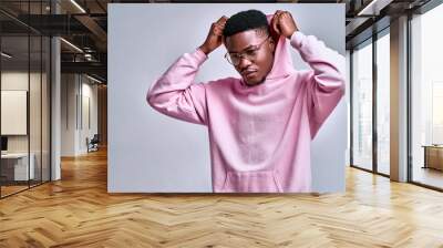 Close up of young african american man in pink streetwear hoodie with hood on head posing isolated on grey background in studio. Wall mural