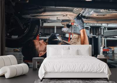 Concentrated auto mechanic male working alone on the floor repairing bottom of the car, look at details, troubleshoot the car. Wall mural