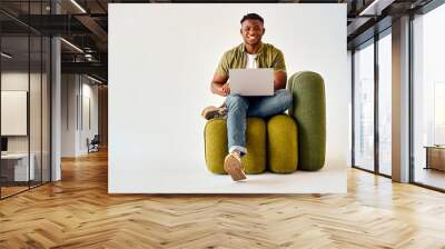 happy african american guy sitting on design chair and holding wireless laptop. male freelancer in c Wall mural