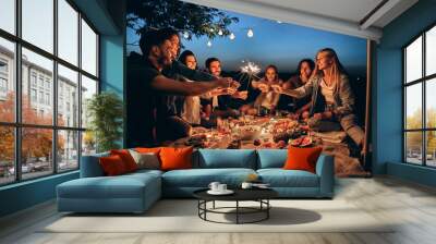 Happy friends having fun with fire sparkles. Young people millennials camping at picnic after sunset. Wall mural