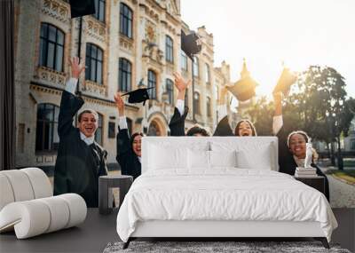 Happy graduates of a college or university throw their mortarboard up to the sky and sincerely rejoice in the fresh air on the campus. Happy future, motivation. Graduation celebration. Wall mural