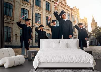 Happy smiling confident graduates standing near university and showing their diplomas.Education and graduating from university or college concept. Wall mural