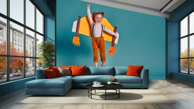 Little child girl with jet cardboard wings is playing and dreaming of becoming a pilot. Wall mural