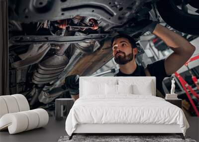 Mechanic examining under the car at the repair garage. Wall mural