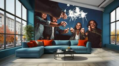 People at night holding sparklers. Group of friends enjoying with sparklers in evening. Wall mural