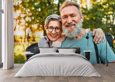 Portrait of active sincere carefree smiling happy modern gray-haired couple shouldering bag with sports mats, man holding water. Sports jogging, training in the park in the morning. Wall mural