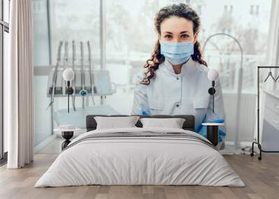 Portrait of female dentist. She standing at her office in mask. Wall mural