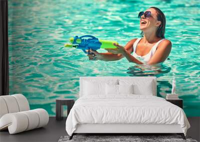 Pretty girl playing with water guns in pool Wall mural