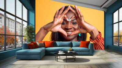 Smiling young african american woman showing shape heart with hands heart-shape sign posing isolated on yellow background in studio. People lifestyle concept. Close up view. Wall mural