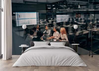 Teamwork. Young focused serious business women and men work in a conference room on a project presentation. Light from a spacious office is reflected through the glass. Wall mural