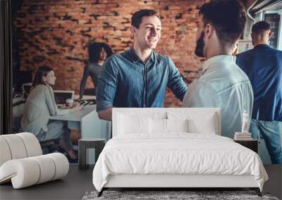 Two happy young men shaking hands while standing in the office Wall mural