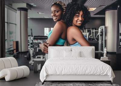 Waist up portrait of two fit young women standing back to back and looking at camera after workout in fitness studio, copy space Wall mural