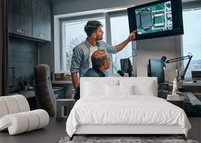 Work in the office. Two men work in a modern office on the development of microchips for the maintenance of electronic devices. The man points to the image of the chip displayed on the monitor. Wall mural