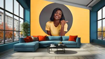 Young beautiful woman wearing yellow t-shirt smiling with happy face looking and pointing to the side with thumb up. Copy space. Wall mural