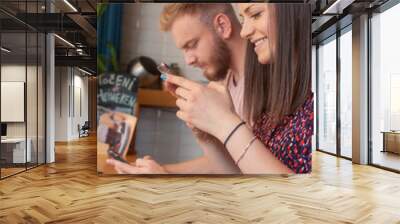 one young woman, using phone, with her friend in background. Sitting in a cafe. Wall mural