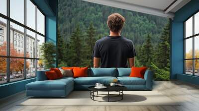 Mock up of a man wearing a plain black t-shirt from behind, with a mountain forest background with dense green trees Wall mural