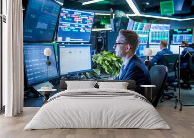 A focused professional in a modern trading room monitors multiple screens displaying financial data and stock market trends, emphasizing concentration and technology in finance. Wall mural