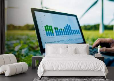 Man analyzing data on laptop in green field with wind turbines, representing renewable energy and sustainable agriculture. Wall mural