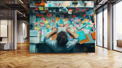 Overhead view of a busy desk cluttered with colorful sticky notes and office supplies, showcasing a creative and chaotic work environment. Wall mural