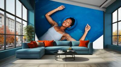 Beautiful middle-aged African American woman floating in tank filled with dense salt water used in meditation, therapy and alternative medicine. Wall mural