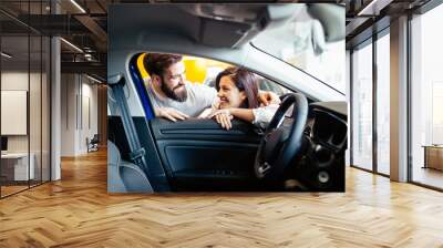 Beautiful young couple at car showroom choosing a new car to buy. Wall mural