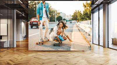 Beautiful young couple enjoying skateboarding on city street. Wall mural