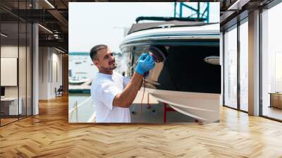 Boat maintenance - Man with orbital polisher polishing boat in marina. Wall mural