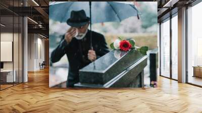 Elegant sad elderly man standing on the rain with umbrella and grieves at the grave of a loved person Wall mural