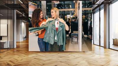 Female seller helps buyer to choose between diferent clothes. Wall mural