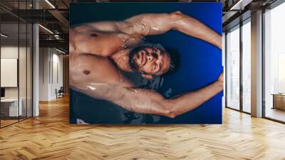 Handsome beard man floating in tank filled with dense salt water used in meditation, therapy, and alternative medicine. Wall mural