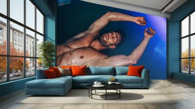 Handsome beard man floating in tank filled with dense salt water used in meditation, therapy, and alternative medicine. Wall mural