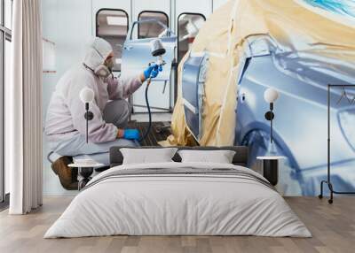 Man with protective clothes and mask painting car using spray compressor. Selective focus.  Wall mural