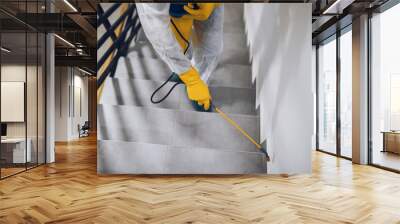 Manual worker in protective work wear spraying virus and bacteria disinfection in residential building with sprayer. Wall mural