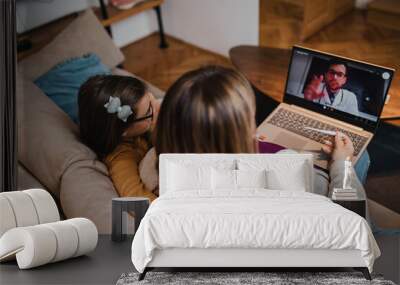 Middle age doctor talking and examining little girl using laptop computer and internet connection. They are chatting while doctor gives health advices. Telehealth concept. Wall mural