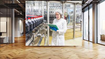 Young happy female worker in bottling factory checking juice bottles before shipment. Inspection quality control. Wall mural