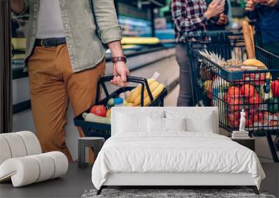 Young man buying groceries at the supermarket. Other customers in background. Consumerism concept. Wall mural