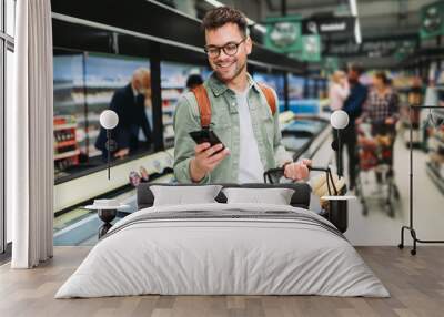 young man buying groceries at the supermarket. other customers in background. consumerism concept. Wall mural